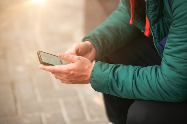 The hands of a young man hold the phone on the street blurred background a guy uses a smartphone to ...