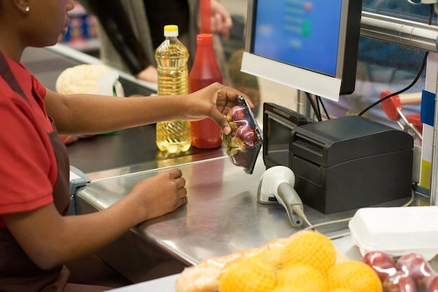 Hands of young saleswoman scanning packed fruit in supermarket