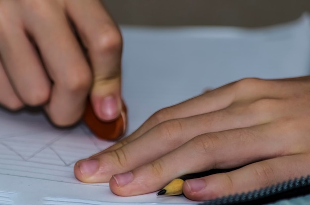 Hands of a young student erasing exercise done on school\
paper