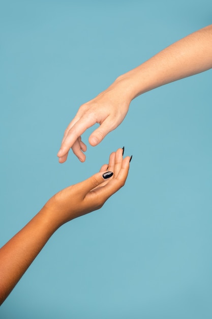 Photo hands of young supportive women of different ethnicities stretching towards each other for sympathy against blue background