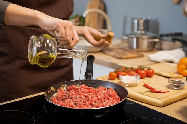 Hands of young woman adding olive oil in minced meat