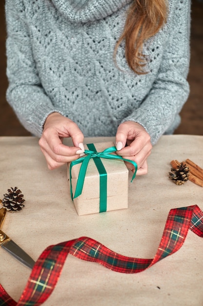 若い女性の手が休日のクリスマスと新年のプレゼントを作成し、梱包します。プレゼントとおめでとうございます。緑のリボンが付いている包帯。水平