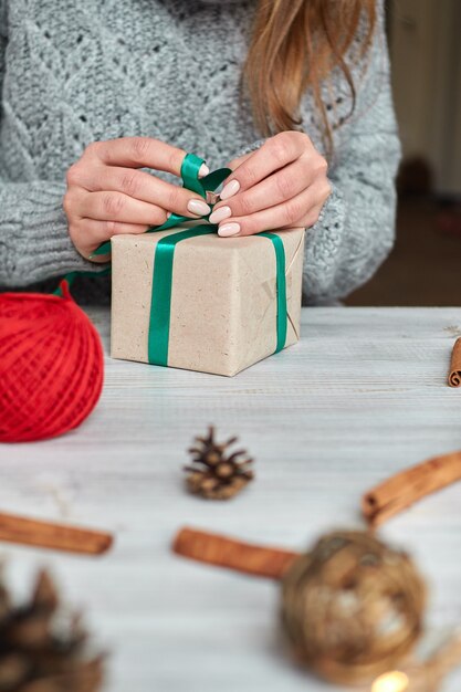 The hands of a young woman create and pack christmas and new year presents for the holiday. presents to relatives and friends with congratulations. bandages with green ribbon