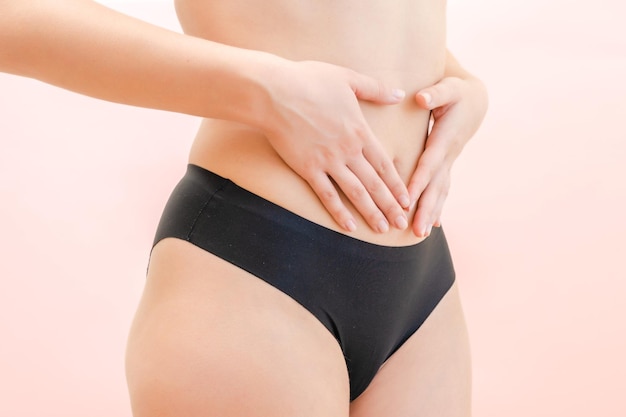 Hands of young woman on her stomach with pink background