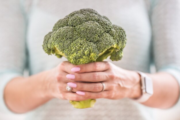 The hands of a young woman hold a fresh broccoli.