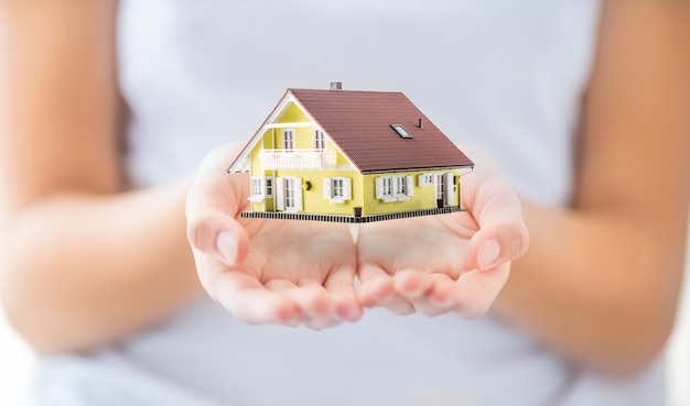 Hands of young woman holding model house.