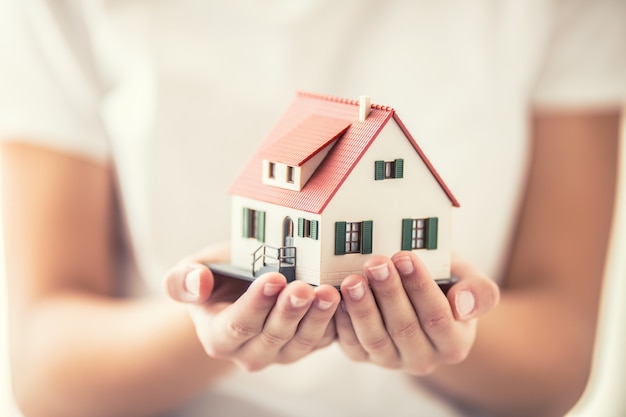 Hands of young woman holding model house.