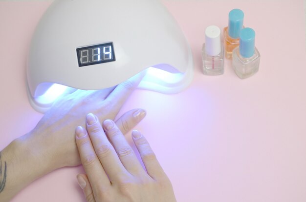 Hands of young woman at manicure procedure close up on pastel pink background