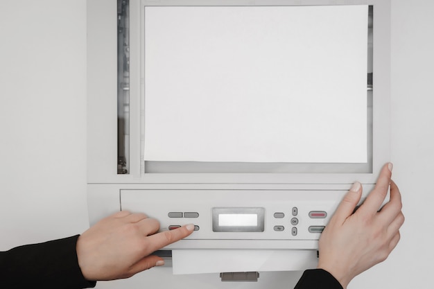 The hands of a young woman placing a piece of paper on a\
flatbed scanner