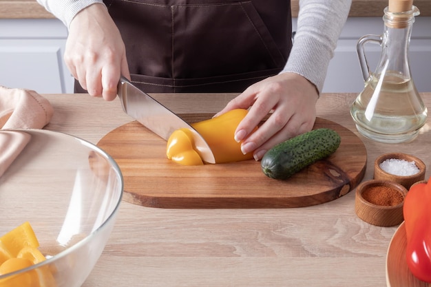 The hands of a young woman slice a vegetable salad on a wooden board and kitchen countertop shortterm plan