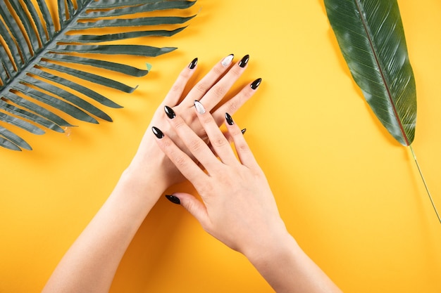 Hands of a young woman at the table with leaves on an orange background