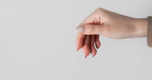 Hands of a young woman with beige nails on a light gray background. Manicure, pedicure beauty salon concept. Copy space for text or logo. Gel polish and an abstract white spider web pattern.