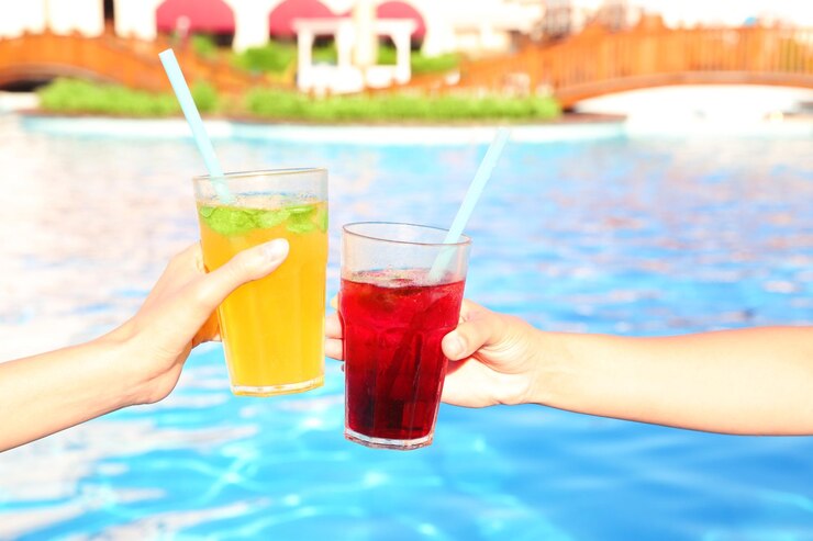 Photo hands of young women clinking glasses with cocktails near pool