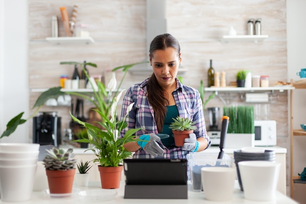 Handschoenen dragen om te tuinieren tijdens het gebruik van een tablet-pc in de keuken thuis en bloemen op tafel