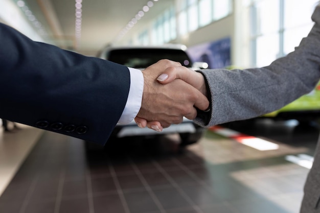 Foto stretta di mano sullo sfondo di una concessionaria di auto a un affare il concetto di acquisto di un'auto in leasing