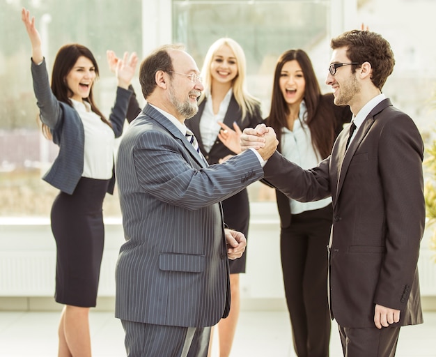 Handshake of business partners on background of cheering business team .