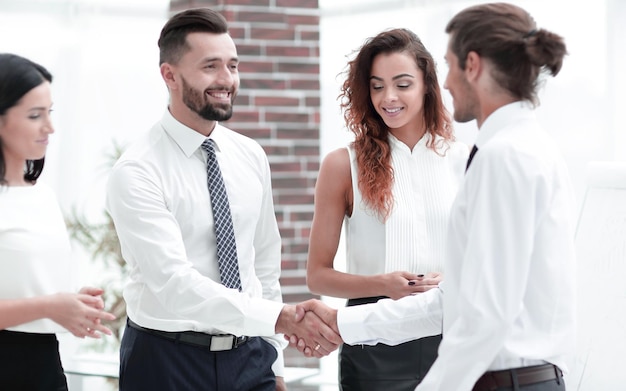 Handshake business partners and business team standing in office