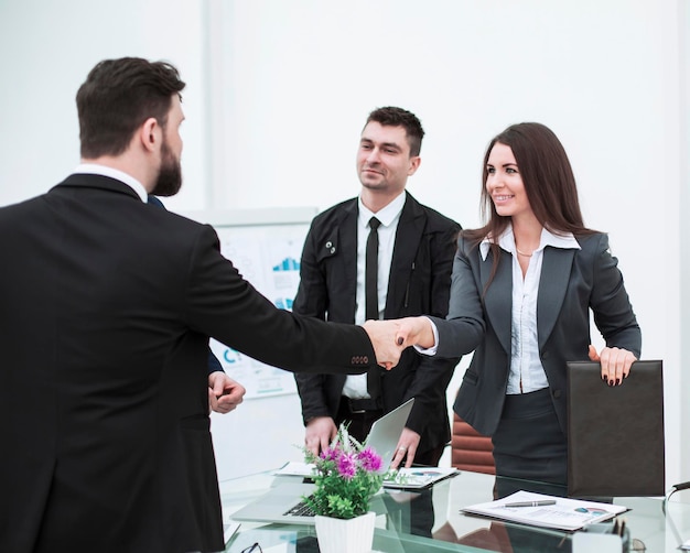 Handshake business partners at the meeting near the desktop in a modern office