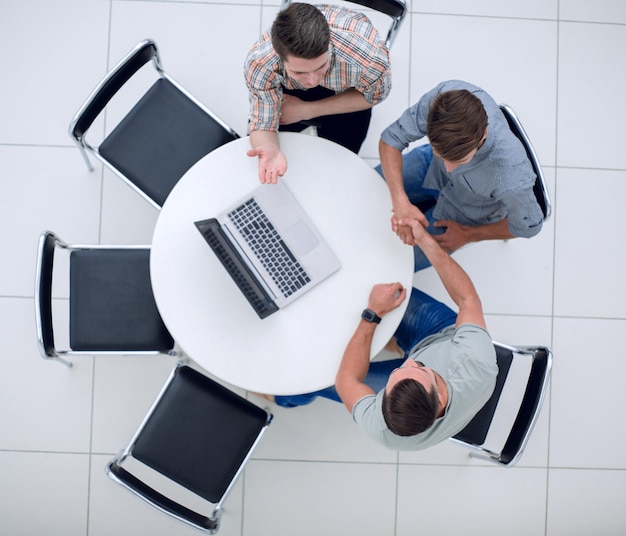 Handshake of the colleagues sitting around the table