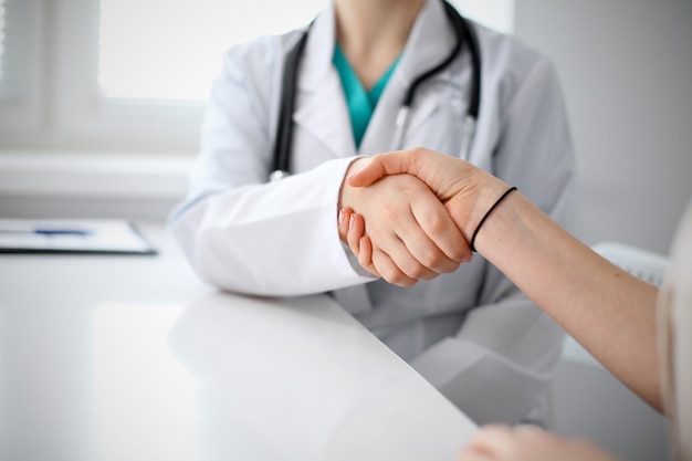 Handshake doctor and patient sitting at the table, closeup.