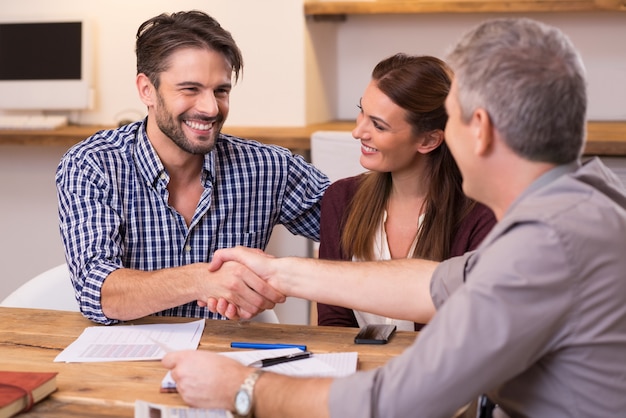 Handshake of a mature manager with a happy young couple at office. Businessmen handshake during meeting signing agreement. Happy man shaking hands whit his finacial advisor.
