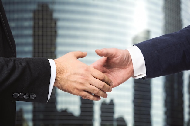 Handshake of two businessmen on the background of office building windows signing of a contract concept close up