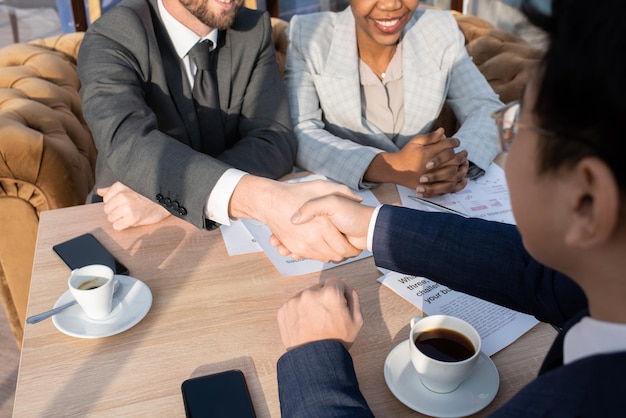 Handshake of two successful business partners over table with papers and cups of coffee