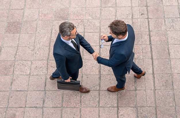 Foto stretta di mano con il partner in città per salutare uomini d'affari in abito che si stringono la mano all'aperto per affari