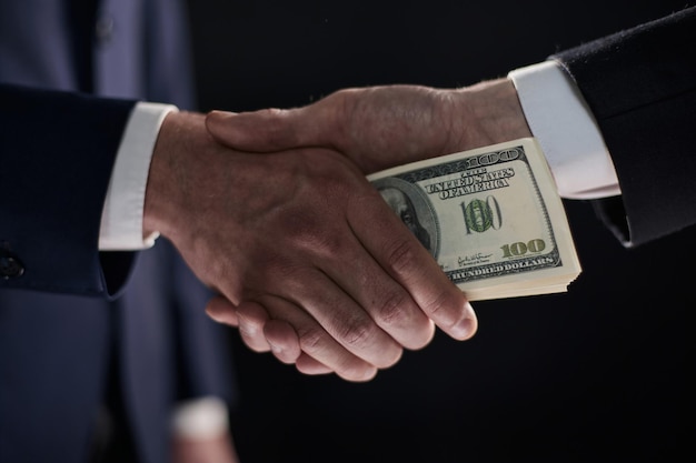 Handshake with the transfer of money on a black background