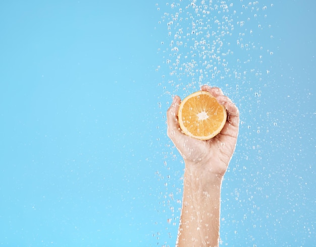 Handsinaasappel en water met natuurlijke huidverzorging voor gezondheid, wellness en biologisch fruit op een blauwe studioachtergrond Schoonheid vers en voedsel voor sappige vitamine C huidverzorgingsbehandeling voor dermatologie