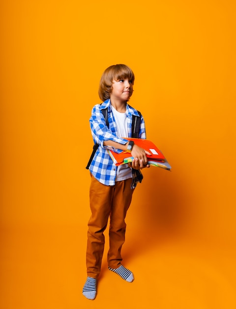 Handsome 7 year old boy with backpack holding books on yellow background for education concept