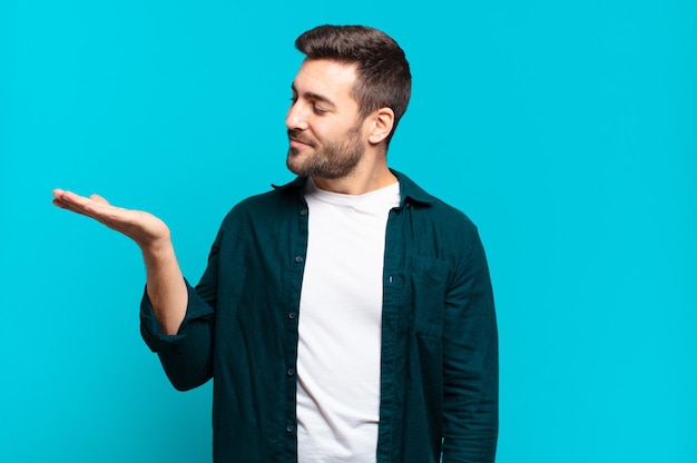 Handsome adult blond man feeling happy and smiling casually, looking to an object or concept held on the hand on the side