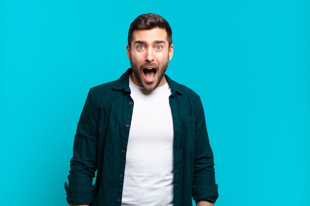 handsome adult blond man feeling terrified and shocked, with mouth wide open in surprise