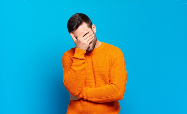 Handsome adult blond man looking stressed, ashamed or upset, with a headache, covering face with hand