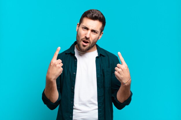 Handsome adult blond man with a bad attitude looking proud and aggressive, pointing upwards or making fun sign with hands