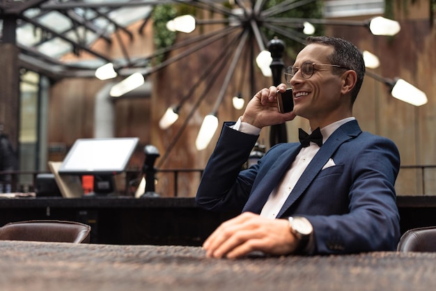 Handsome adult man in suit talking by phone at restaurant