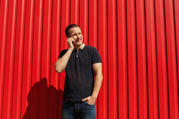 Handsome adult man using his cellphone, talking on red wall