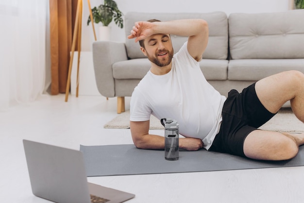집에서 운동하는 동안 휴식을 취하는 동안 노트북과 식수를 사용하는 잘 생긴 성인 남자