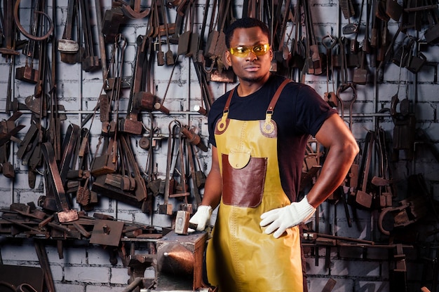 Handsome african americam man forging steel next to furnace in dark workshop small business comcept and protective glasses with glovesconcept save work