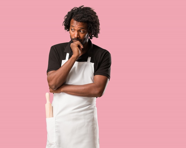 Handsome african american baker doubting and confused, thinking of an idea or worried about something