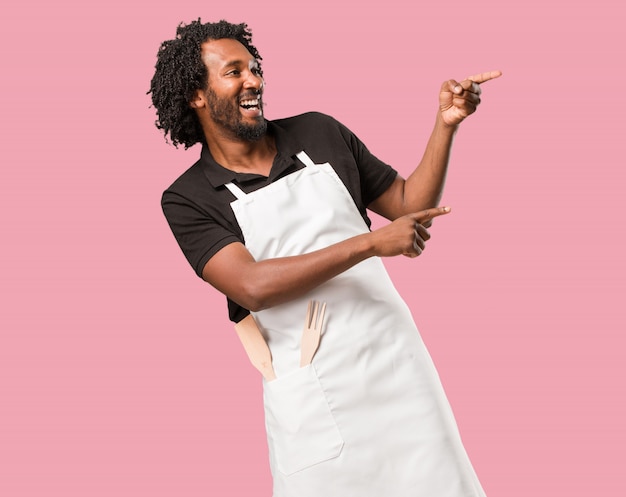 Handsome african american baker pointing to the side, smiling surprised presenting somethi