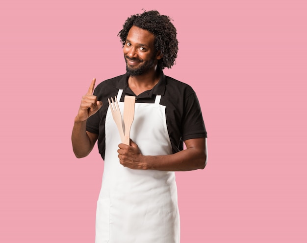 Handsome african american baker showing number one, symbol of counting, concept of mathema