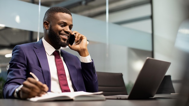 電話で会話するラップトップに取り組んでいるハンサムなアフリカ系アメリカ人のビジネスマン