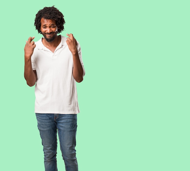 Handsome african american crossing his fingers, wishes to be lucky for future projects