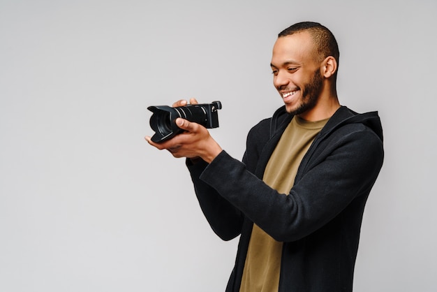 Красивый афро-американский парень держит цифровой фотоаппарат над светло-серой стеной