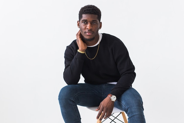 Handsome African American man posing in black sweatshirt on a white surface. Youth street fashion