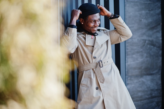 Handsome african american man posing outside in black hat and beige coat.