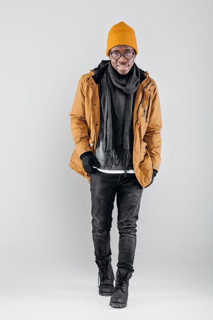 Handsome African-American man in yellow hat and jacket posing on gray background