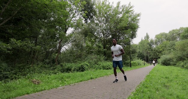 야외에서 슬로우 모션으로 운동하는 잘생긴 아프리카계 미국인 스포츠맨. 운동복을 입은 남자가 공원의 나무들 사이를 달리고 있습니다. 건강한 라이프 스타일의 개념입니다.