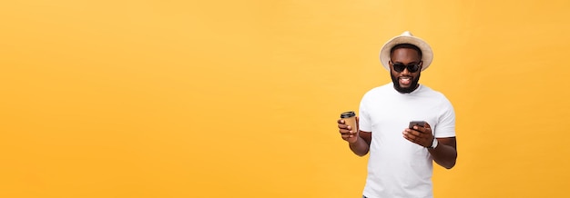 Handsome african american with mobile phone and take away coffee cup isolated over yellow gold background